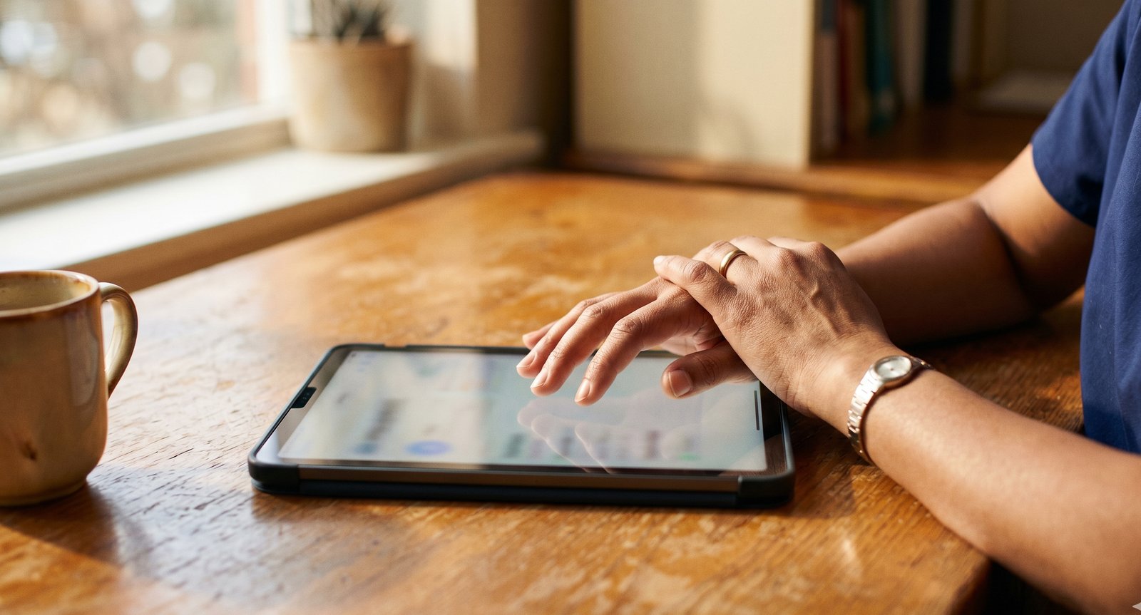 A nurse using a tablet at a desk with morning light